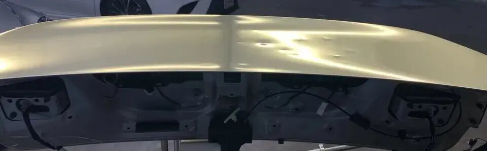 Close-up of a PDR technician inspecting a roof panel with reflection lighting
